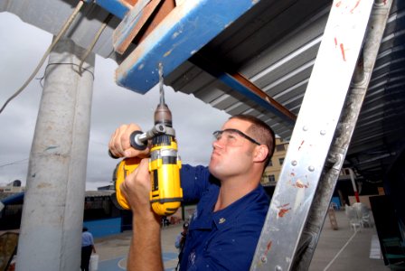 US Navy 070819-N-8704K-038 U.S. Coast Guard Health Services Technician 2nd Class Drew Schultz, attached to hospital ship USNS Comfort (T-AH 20), drills a hole in preparation for new lighting at the Luis Teodoro Cantos School