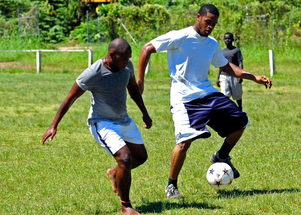 US Navy 070819-N-1752H-113 Aviation Boatswain's Mate (Handling) 3rd Class Delron Cowan, right, maneuvers around defenders during a community relations soccer game between local youth and Sailors from USS Peleliu (LHA 5) in supp