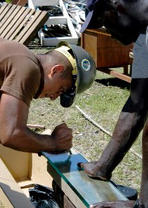 US Navy 070823-N-9195K-061 A local volunteer assists Construction Electrician 3rd Class Serafin Avila, attached to Naval Mobile Construction Battalion (NMCB) 7, as he cuts panes of glass that will be used as window slats