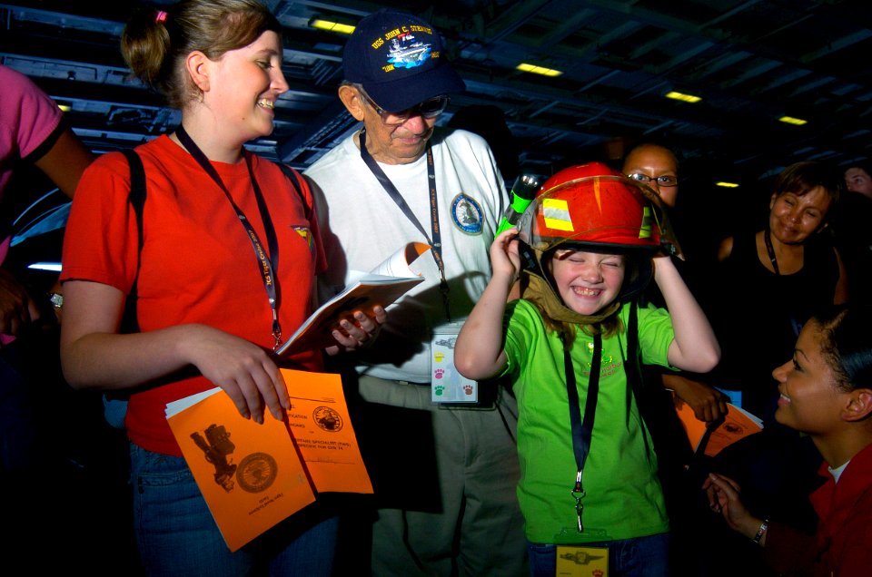US Navy 070822-N-3038W-181 Damage Controlman 3rd Class Felicity Prestianni, right, from engineering department's damage control division, helps a young Tiger try on a firefighting helmet that is part of a fire fighting ensemble