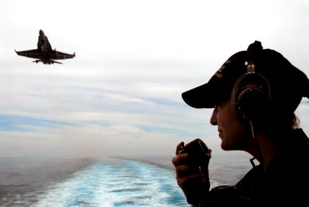 US Navy 070825-N-0890S-072 Seaman Monica Kreinheder talks on a sound-powered phone while standing aft lookout as an F-A-18C Hornet prepares to land on the flight deck of the nuclear-powered aircraft carrier USS Nimitz (CVN 68)