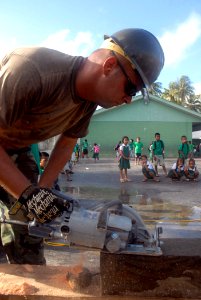 US Navy 070830-N-4267W-010 Schoolchildren watch as Builder 2nd Class Mike Carman, with Naval Mobile Construction Battalion (NMCB) 7, uses a circular saw to cut out posts to be used as a frame for a new playground at Rairok Elem