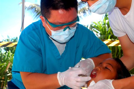 US Navy 070831-N-6410J-129 Lt. Cmdr. Paul Lim removes a young girl's tooth during a dental civic action program photo