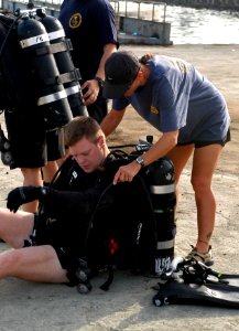US Navy 070911-F-0827S-003 Chief Explosive Ordnance Disposal Technician Melissa Tackitt helps Lt. Eric Vik into his dive equipment before performing a force protection dive of one of the piers at the Djibouti port