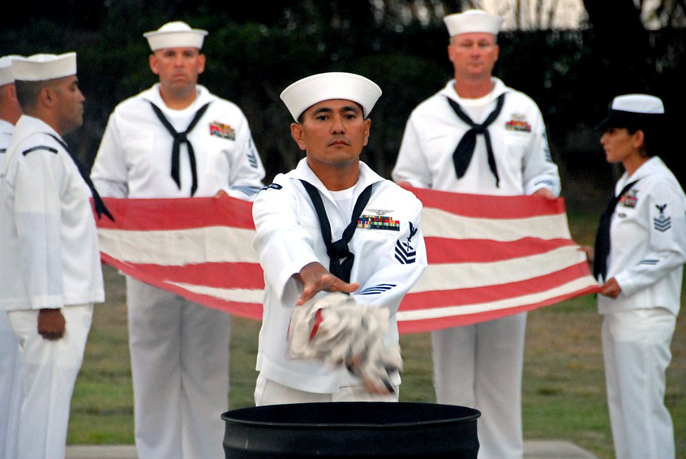 US Navy 070911-N-1722M-200 Aviation Machinist's Mate 1st Class Alfredo Naferrete drops a portion of an American flag into a burn barrel during a flag retirement ceremony