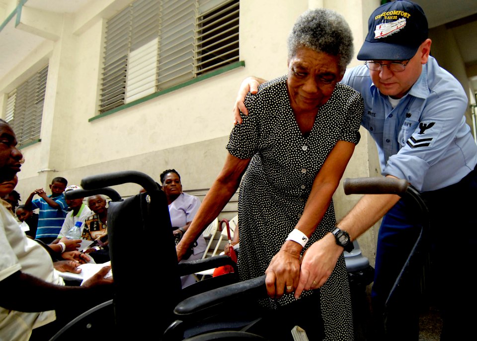 US Navy 070919-N-6278K-182 Electronics Technician 2nd Class Mark White, attached to Military Sealift Command hospital ship USNS Comfort (T-AH 20), assists a patient into her wheelchair at Moulton Hall Methodist Primary School