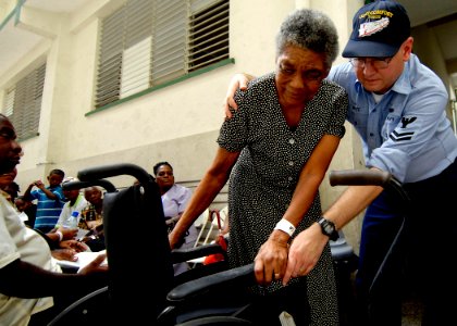 US Navy 070919-N-6278K-182 Electronics Technician 2nd Class Mark White, attached to Military Sealift Command hospital ship USNS Comfort (T-AH 20), assists a patient into her wheelchair at Moulton Hall Methodist Primary School photo