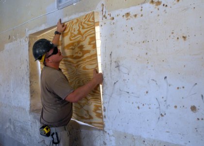US Navy 070922-N-3560G-024 Builder 3rd Class Anthony Reeder, attached to Naval Mobile Construction Battalion (NMCB) 4, uses a sheet of plywood to seal an opening in a wall during the conversion of an old Iraqi prison photo