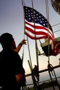 US Navy 071003-N-4774B-017 Quartermaster 2nd Class Jesus Aguilar lowers the national ensign at sunset aboard amphibious assault ship USS Tarawa (LHA 1)