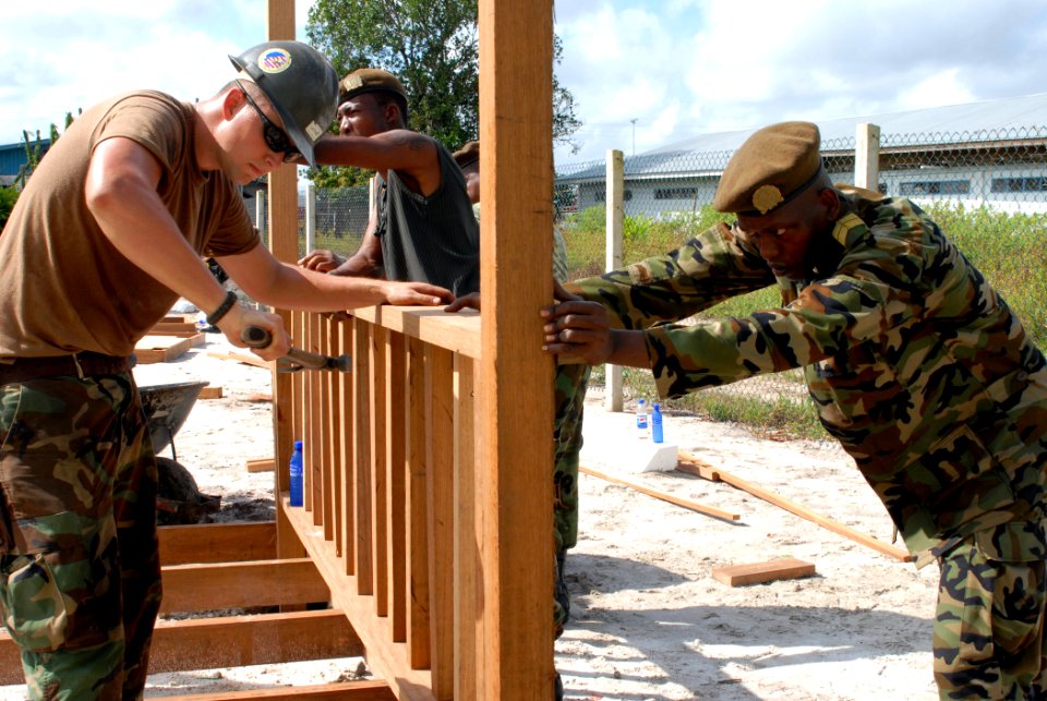 US Navy 071004-N-7092S-028 Builder 2nd Class William Lathan, a Seabee assigned to Military Sealift Command hospital ship USNS Comfort (T-AH 20), drives a nail into a gazebo while Cpl. Eugene Van Leyded, a soldier with the Surin photo