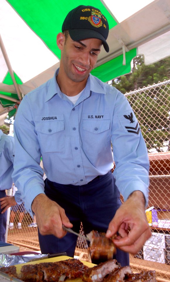 US Navy 071102-N-9758L-059 Culinary Specialist 2nd Class Nicholas Josshua, assigned to Arleigh Burke-class guided-missile destroyer USS Chafee (DDG 90), cuts up some barbecued ribs for the Barbecue Cook-off Competition held at