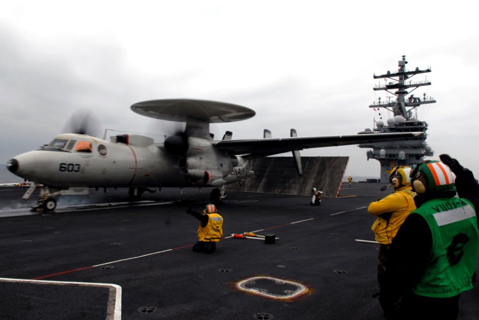 US Navy 071108-N-0555B-087 Flight deck personnel look on, waiting to reset the catapult as an E-2C Hawkeye, assigned to the Golden Hawks of Airborne Early Warning Squadron (VAW) 112, launches from the flight deck