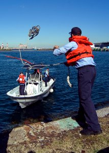 US Navy 071113-N-5253W-001 Mass Communication Specialist Seaman Apprentice Anthony Martinez, assigned to aircraft carrier USS Kitty Hawk (CV 63), tosses a line to a port operations boat while retrieving a section of retaining b
