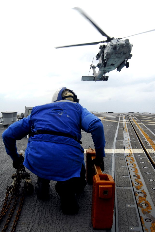 US Navy 071121-N-3136P-049 A boatswain's mate stands ready with chock and chains to secure an SH-60F Seahawk, from Helicopter Anti-submarine Squadron (HS) 14, as it lands aboard the flight deck of guided-missile destroyer USS M