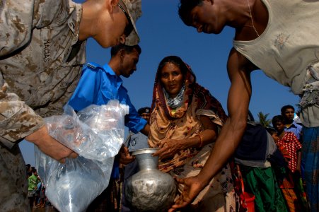 US Navy 071128-N-5642P-037 A U.S. Marine, assigned to the 22nd Marine Expeditionary Unit (Special Operations Capable), pours water into a jug brought to him by local Bangladesh woman photo