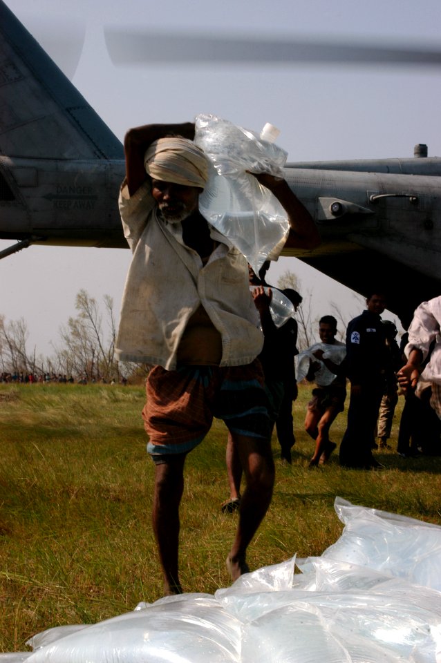 US Navy 071127-N-5642P-189 A local resident carries a bag of fresh water off of the CH-53E Sea Stallion helicopter that is there delivering relief supplies