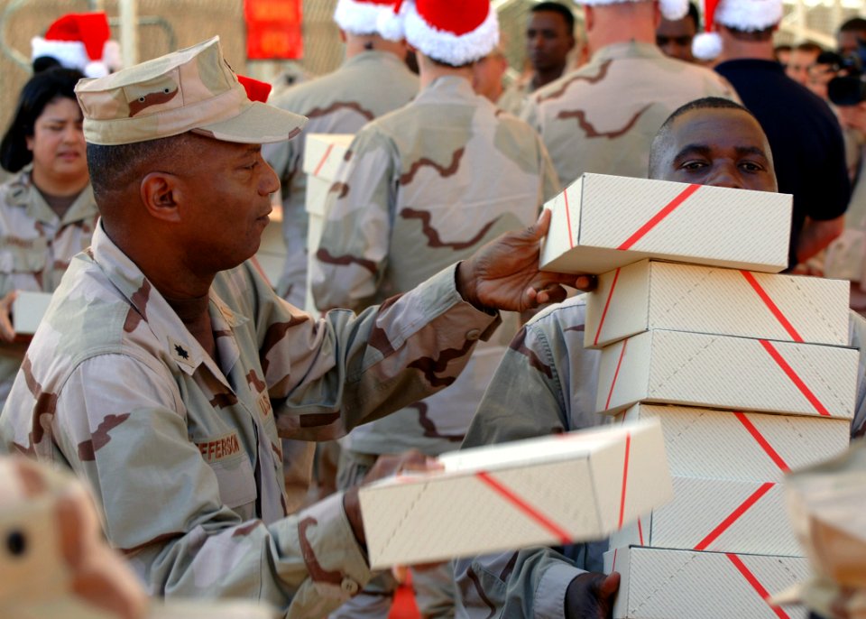 US Navy 071204-N-3285B-063 A Sailor with a team of volunteers delivering gifts to the 5th Fleet area of responsibility piles gift boxes on to a service member deployed to Combined Joint Task Force-Horn of Africa