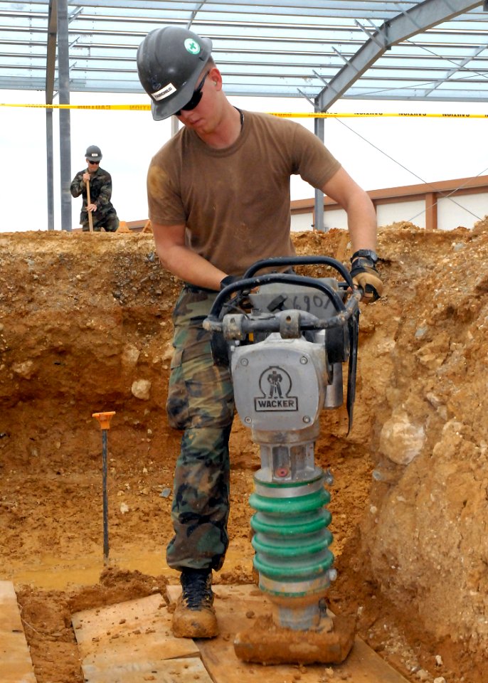 US Navy 071217-N-8547M-043 uilder 2nd Class Lance D. Fairchild of Naval Mobile Construction Battalion (NMCB) 5 packs the loose dirt after setting the elevation for footers