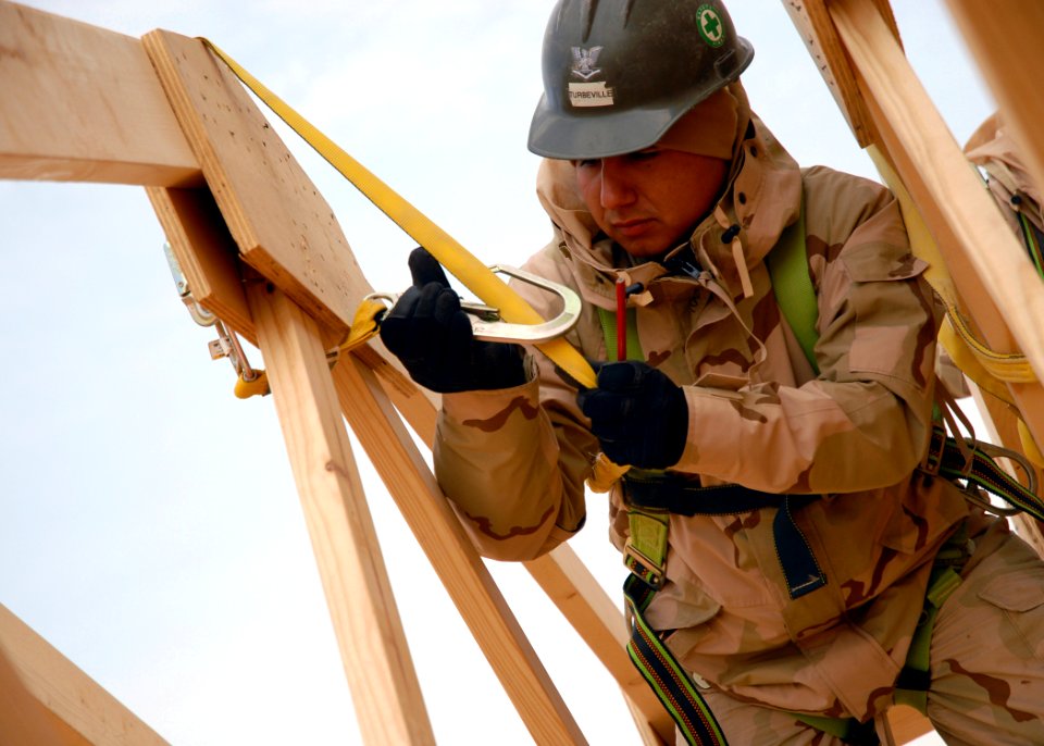 US Navy 071221-N-3857R-007 Builder 3rd Class Adam Turbeville, assigned to Naval Mobile Construction Battalion (NMCB) 1, connects his safety harness to a truss while working on the construction of a fellowship hall
