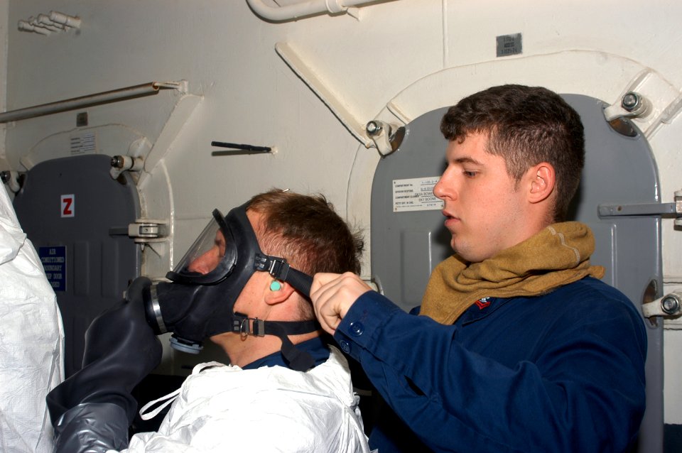 US Navy 071223-N-5033P-012 Damage Controlman 2nd Class Petty Officer Nathan Stachey assists a Sailor in donning an in-line Self Contained Breathing Apparatus during a simulated toxic gas casualty drill