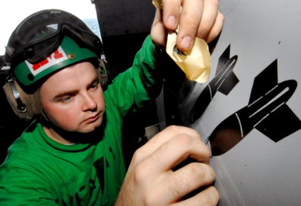 US Navy 080104-N-2984R-043 Aviation Structural Mechanic 3rd Class Michael Grossi assigned to the Red Rippers of Strike Fighter Squadron (VFA) 11 removes tape from a freshly painted ordinance symbol on the side of an F-A-18 Supe