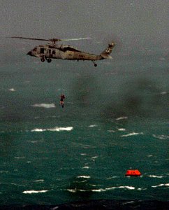 US Navy 071223-N-1688B-043 A Navy Search and Rescue swimmer descends from an MH-60S Seahawk helicopter to retrieve survivors from a life raft at sea