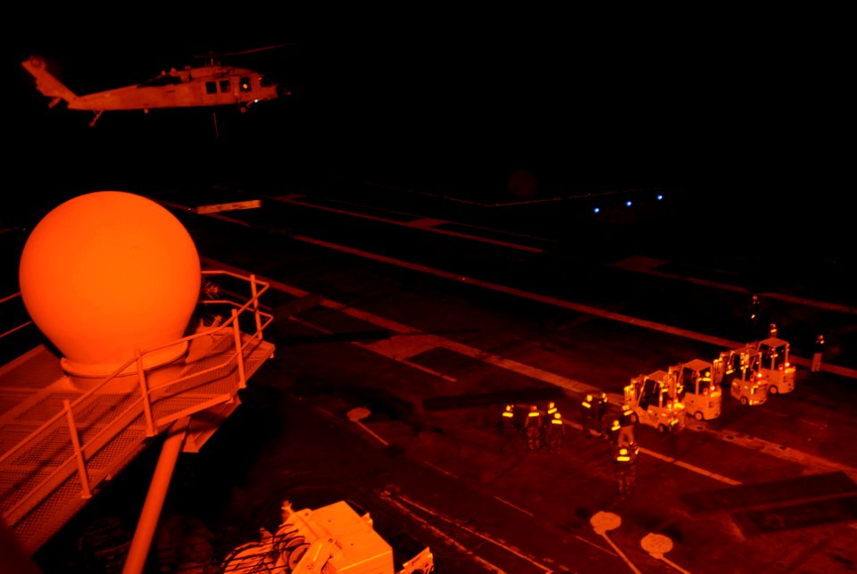 US Navy 080108-N-1635S-001 Sailors from USS Ronald Reagan (CVN 76) work into the night as an MH-60S Seahawk, assigned to Helicopter Sea Combat Squadron (HSC) 21, lowers a missile case onto the flight deck during an ammunition o