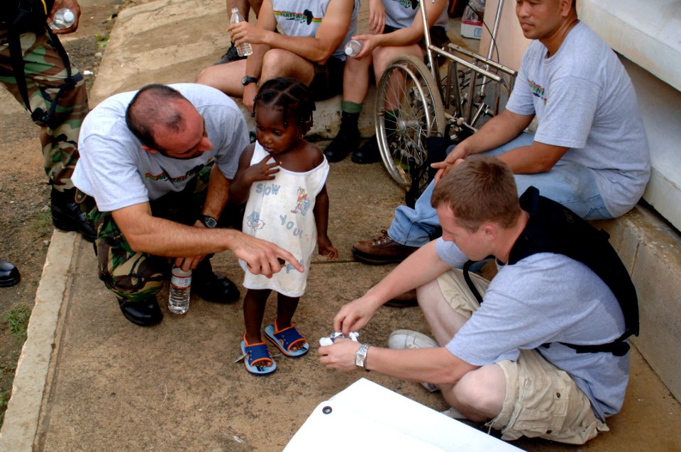 US Navy 080121-N-1429M-164 frica Partnership Station (APS) Sailor Storekeeper 3rd Class Cory Brown, right, helps a local Sao Tomean girl pick out a pair of shoes as APS Portuguese translator Lt. Luis Miguel translates for the t