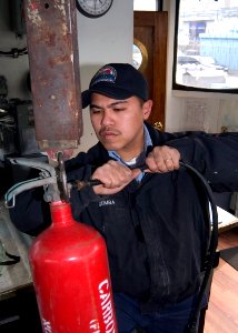 US Navy 080128-N-9520G-003 Boatswain's Mate 2nd Class Gilbert Gumba weighs a carbon dioxide bottle during preventive maintenance for an inspection and survey