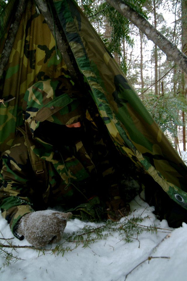 US Navy 080203-N-0411D-048 A student at the Navy Survival, Evasion, Resistance and Escape (SERE) school builds an improvised shelter with a poncho and natural materials