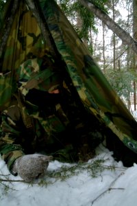 US Navy 080203-N-0411D-048 A student at the Navy Survival, Evasion, Resistance and Escape (SERE) school builds an improvised shelter with a poncho and natural materials