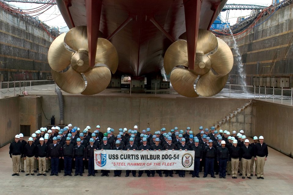 US Navy 080219-N-9520G-001 Sailors assigned to the Arleigh Burke-class guided-missile destroyer USS Curtis Wilbur (DDG 54) pose for a command photo under the ship's screws as the command wraps up a dry dock selective restricted