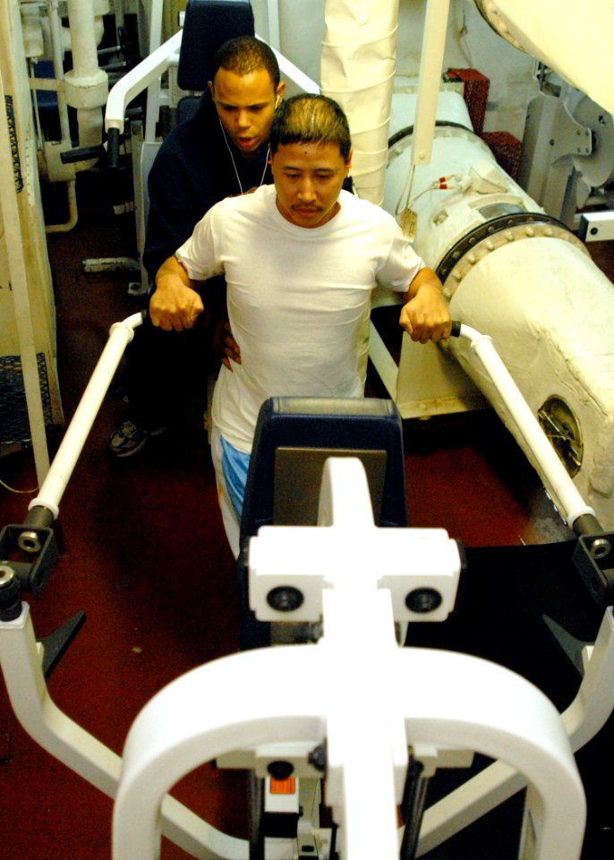 US Navy 080217-N-5476H-074 Culinary Specialist 1st Class Henrie Cosme is assisted by Culinary Specialist 3rd Class Angel Martea workout in the weight room aboard the guided-missile cruiser USS Lake Erie (CG 70)