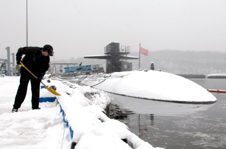 US Navy 080222-N-8467N-004 Storekeeper 2nd Class Mike Hyatt shovels off the pier next to the Los Angeles-class fast-attack submarine USS Philadelphia (SSN 690) on a blustery, snowy morning photo