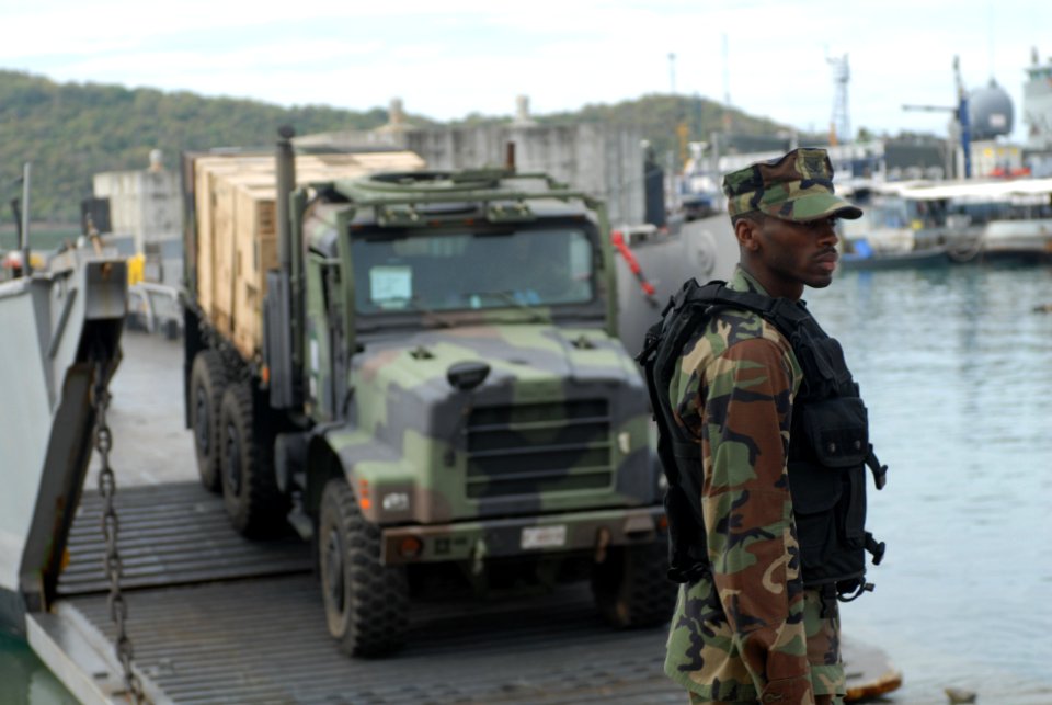 US Navy 080609-N-6936D-064 Boatswain's Mate 3rd Class Draifius Harris, assigned to Beachmaster Unit (BMU) 1, coordinates the movement of trucks and equipment to Landing Craft Utility (LCU) 1627
