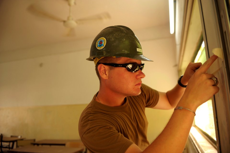 US Navy 080613-N-3674H-077 Steelworker 2nd Class Justin Johnson, assigned to Naval Mobile Construction Battalion (NMCB) 74, tapes a window frame before painting a classroom at the Boulaos Middle School l in Djibouti