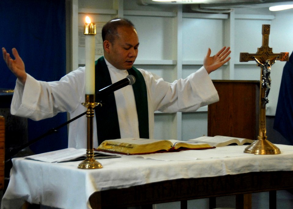 US Navy 080615-N-1281H-004 haplain Lt. Peter Le raises his hands in prayer during a Sunday morning Catholic service