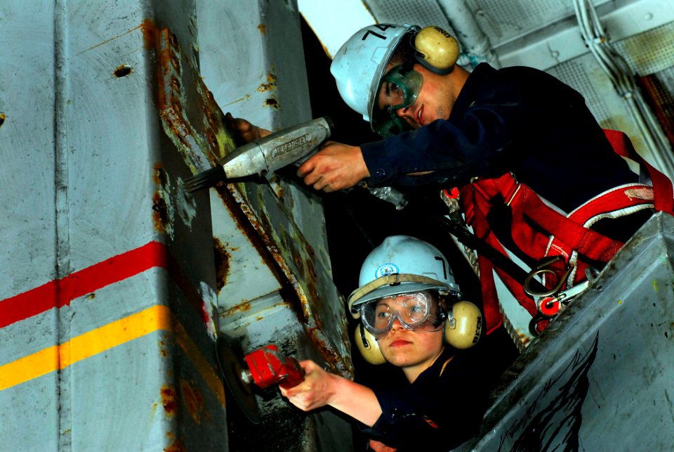 US Navy 080627-N-2610F-007 Seaman Tyler Nash, right, and Seaman Erin Koecke grind rust from a sliding pad-eye in the hangar bay aboard the Nimitz-class aircraft carrier USS John C. Stennis (CVN 74)