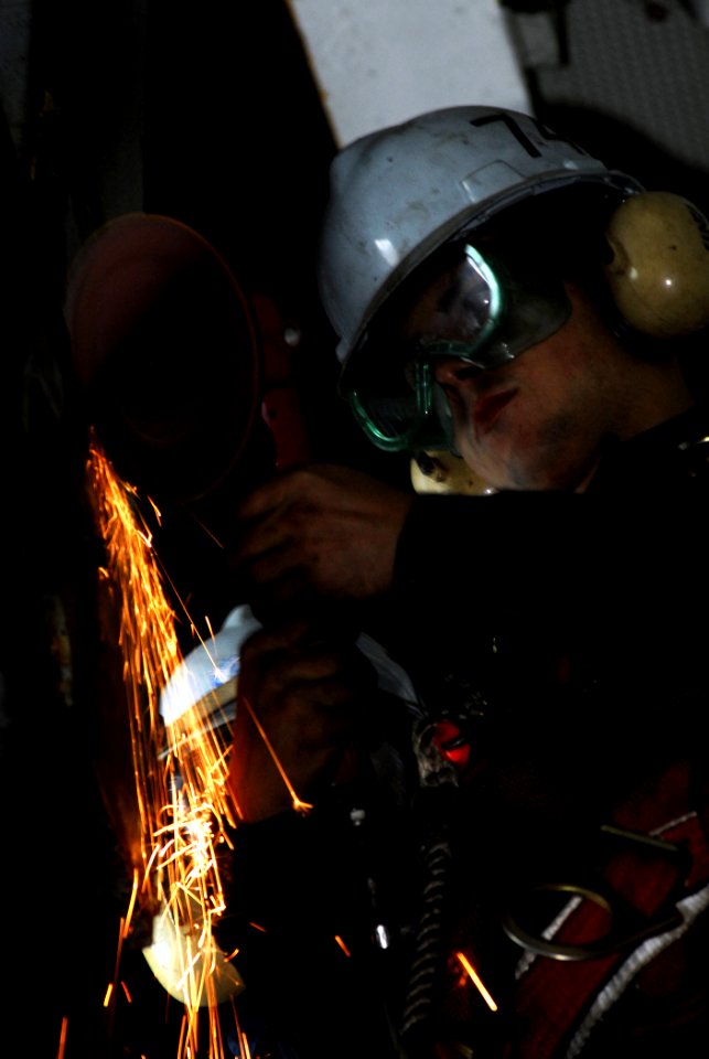 US Navy 080627-N-2610F-011 Seaman Tyler Nash grinds rust from a sliding pad-eye in the hangar bay aboard the Nimitz-class aircraft carrier USS John C. Stennis (CVN 74)