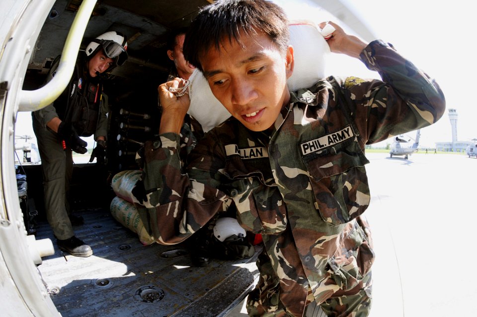US Navy 080630-N-5961C-014 A soldier from the Armed Forces of the Philippines carries a 100-pound bag of rice to a helicopter assigned to the