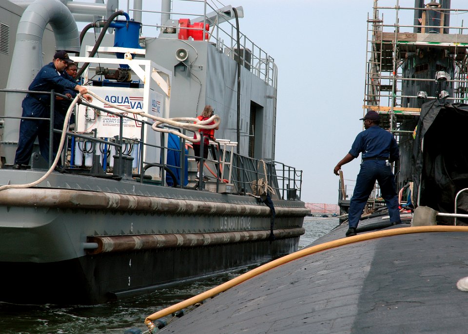 US Navy 080627-N-7668G-057 Electrician's Mate 2nd Class Michael P. Ojea Sr. throws a line to Hull Technician 2nd Class Lemar Carter to moor a Scheduled Preservation Upkeep Coordinated Effort (SPRUCE) Barge
