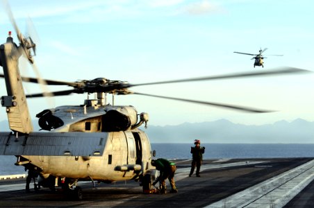US Navy 080701-N-5961C-004 An SH-60F Seahawk flies off in the distance as crewmen and maintenance crews assigned to Helicopter Anti-Submarine Squadron (HS) 4 prepare a second helicopter for launch from the aircraft carrier USS