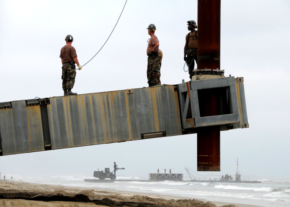 US Navy 080709-N-1424C-497 An Elevated causeway support pile is lowered into place as a Navy lighterage causeway ferry is offloaded in the distance during Joint Logistics Over-The-Shore (JLOTS) 2008