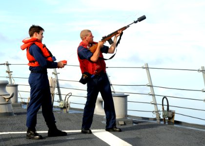 US Navy 080709-N-1082Z-005 Gunner's Mate 3rd Class Marcus W. Stapert, assisted by Operations Specialist 3rd Class Drew Hanna, shoots line across the bow of the guided-missile destroyer USS Ramage (DDG 61)