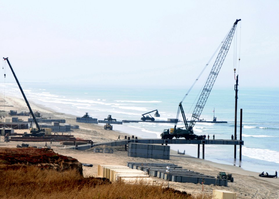 US Navy 080711-N-1424C-965 The Joint Logistics Over-The-Shore 2008 beachhead is expanded by an elevated causeway as support piles are driven into the beach while a Navy lighterage is off loaded in the distance