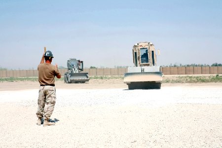 US Navy 080719-N-9623R-001 Equipment Operator 1st Class Bryan Anselmi, assigned to Naval Mobile Construction Battalion (NMCB) 17, guides as Equipment Operator 2nd Class Lucinda Hale operates a compaction roller to level a weapo photo
