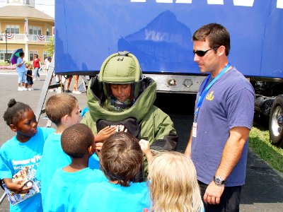 US Navy 080722-N-2888Q-009 Explosive Ordnance Technician Mike Smoot, right, oversees a young girl wearing an EOD 9 bomb disposal suit during Healthy Kids Day at the Delaware State Fair