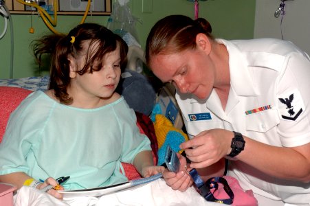 US Navy 080722-N-7975R-001 Personnel Support 3rd Class Jessica White shows a patient at A.I. DuPont Hospital for Children how to attach a Navy lanyard to her cell phone