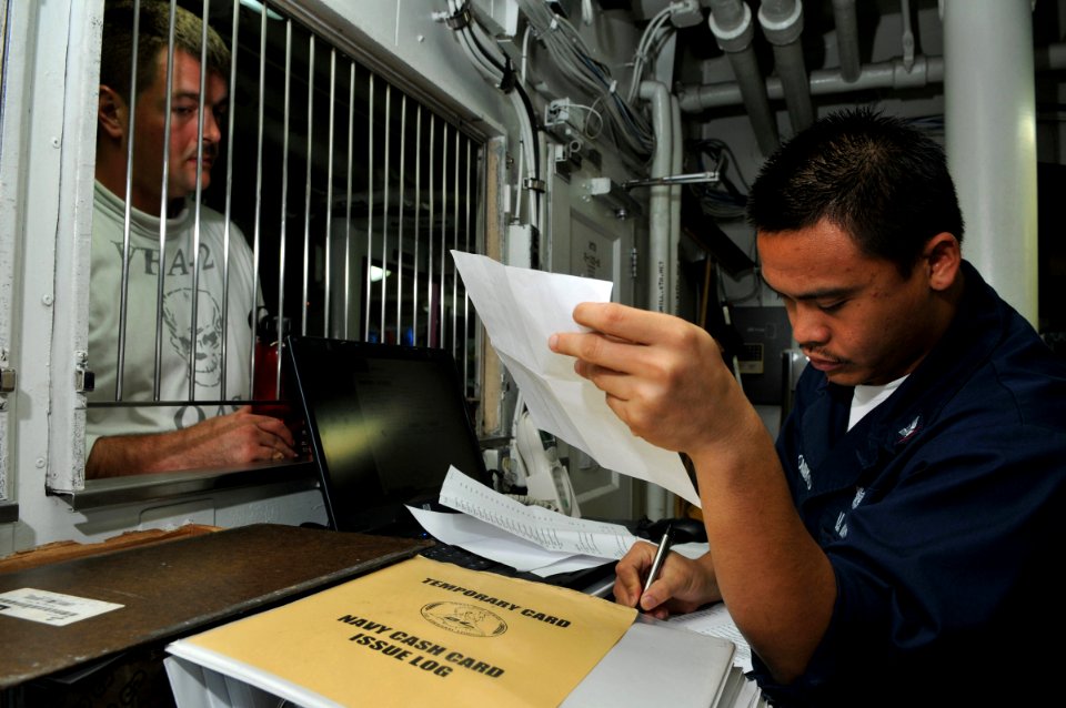 US Navy 080731-N-7981E-032 Personnel Specialist 3rd Class Ferdirick Domingo, from San Diego, Calif., assists a Sailor with his Navy cash card account in the disbursing office aboard the Nimitz-class aircraft carrier USS Abraham
