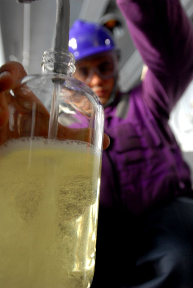 US Navy 080815-N-7730P-049 Aviation Boatswain's Mate (Fuels) 3rd Class Jeremy Curtis fills a sample bottle used for testing fuel purity